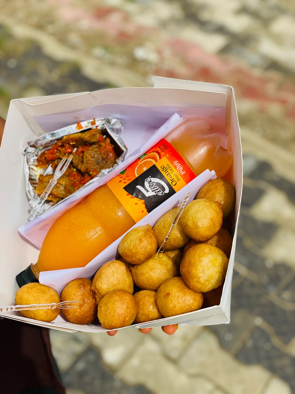 Puff-puff box with peppered beef and a chilled orange juice drink