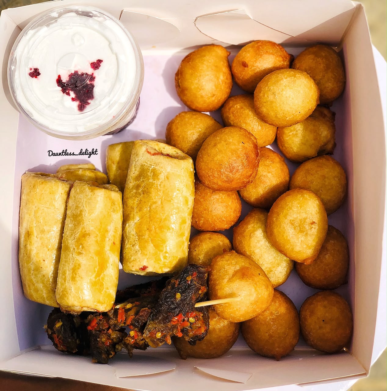 Pastry box with sausage rolls, puff-puff, peppered beef and a parfait cup